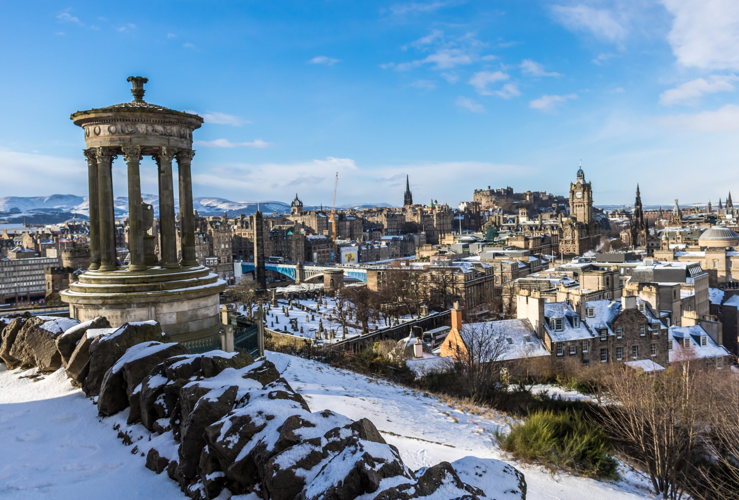 A snowy Edinburgh skyline under a bright blue sky.